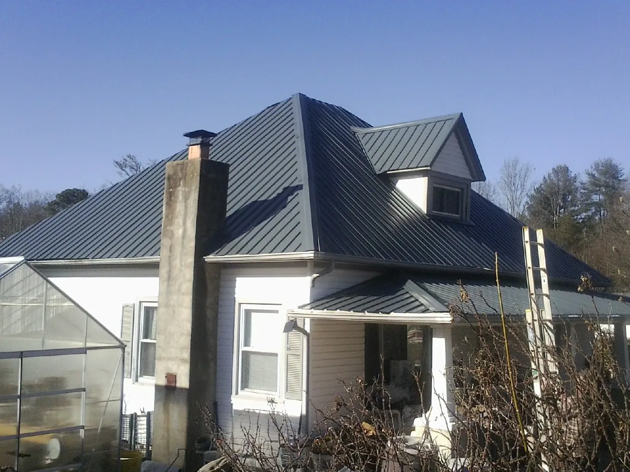 Dark blue standing seam metal roof on a white farmhouse with dormer — Slate & Tile Roof Repair by Roofing Brothers in Chappell Hill