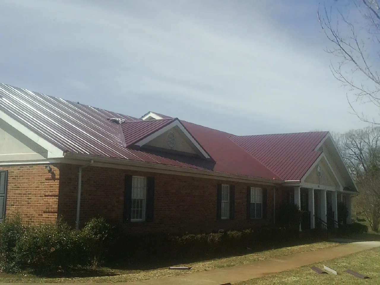 Red metal roof with gabled entries on a long brick building, from a Hail Damage Roof Repair job in Chappell Hill