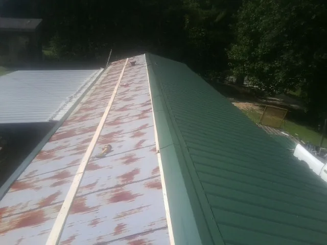 Old rusted panels beside newly installed green metal roofing — Wind Damage Roof Repair by Roofing Brothers in Chappell Hill