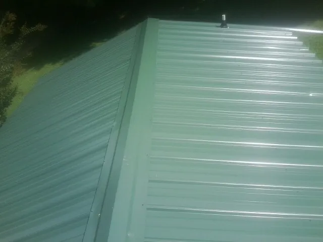 New green metal panels meeting at the ridge of a roof — Flat Roof Repair work by our crew in Chappell Hill