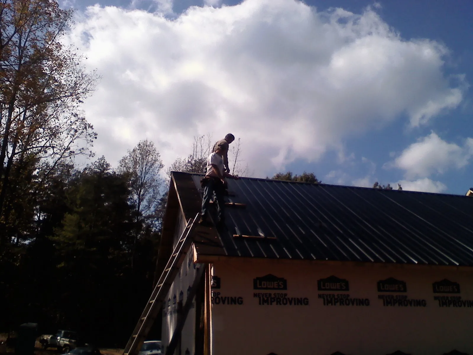 Roofer fastening dark metal panels high against a cloudy sky, from a Roof Inspection job in Chappell Hill