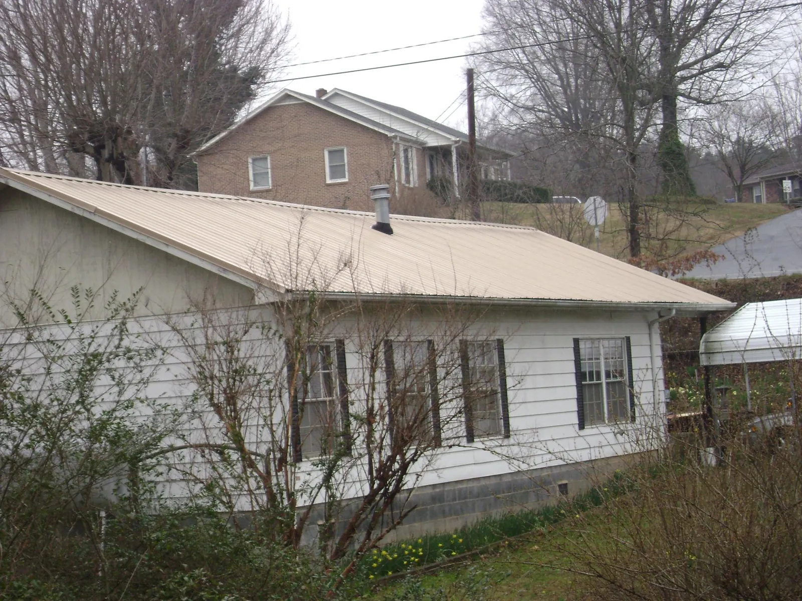 Tan metal roof on a white sided house set into a hillside — Commercial Roofing by Roofing Brothers in Chappell Hill