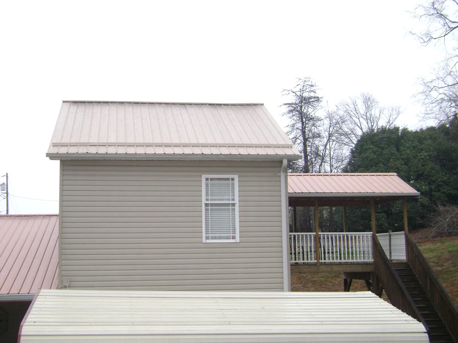 Tan metal roofs on a two story addition and attached porch, from a Roof Replacement job in Chappell Hill