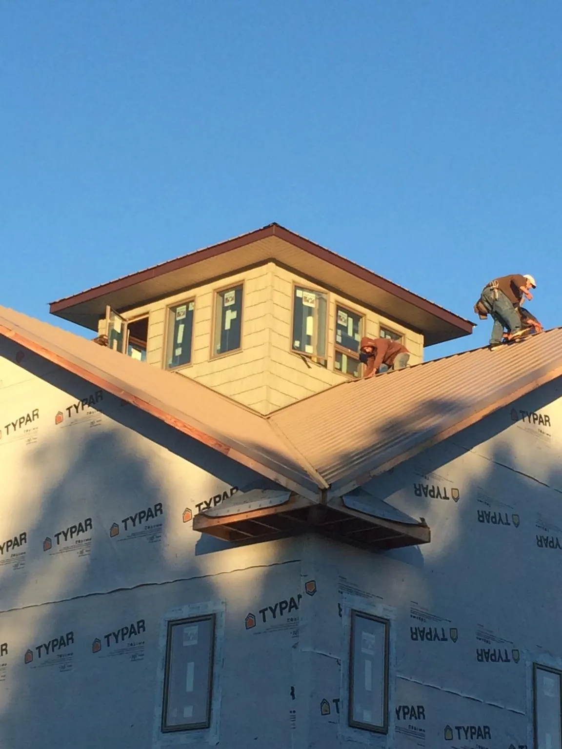 Roofers working around a rooftop cupola on a new metal roof at sunset — Roof Waterproofing in Chappell Hill by Roofing Brothers